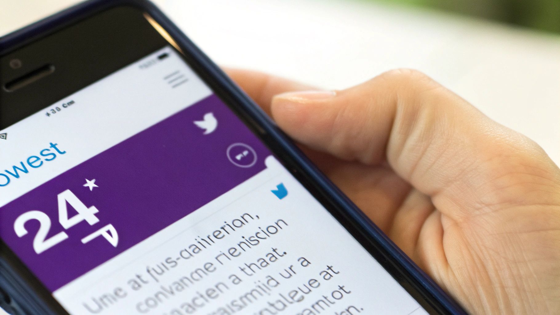Close-up of a person's hand holding a smartphone displaying a social media app with a Twitter logo and text.