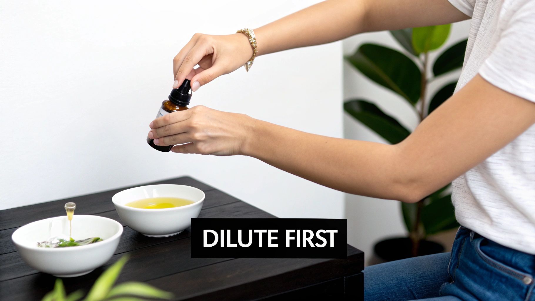 Hands pour essential oil from a dropper bottle into a bowl on a dark table, with text 'DILUTE FIRST'.