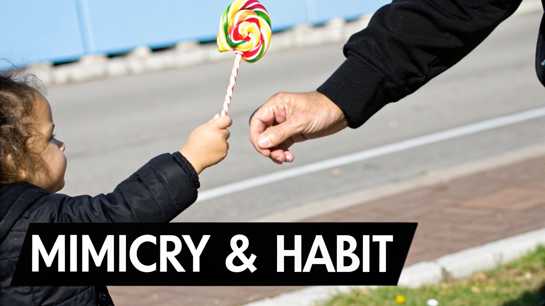A small child in a black jacket offers a bright, swirled lollipop to an adult hand outdoors.