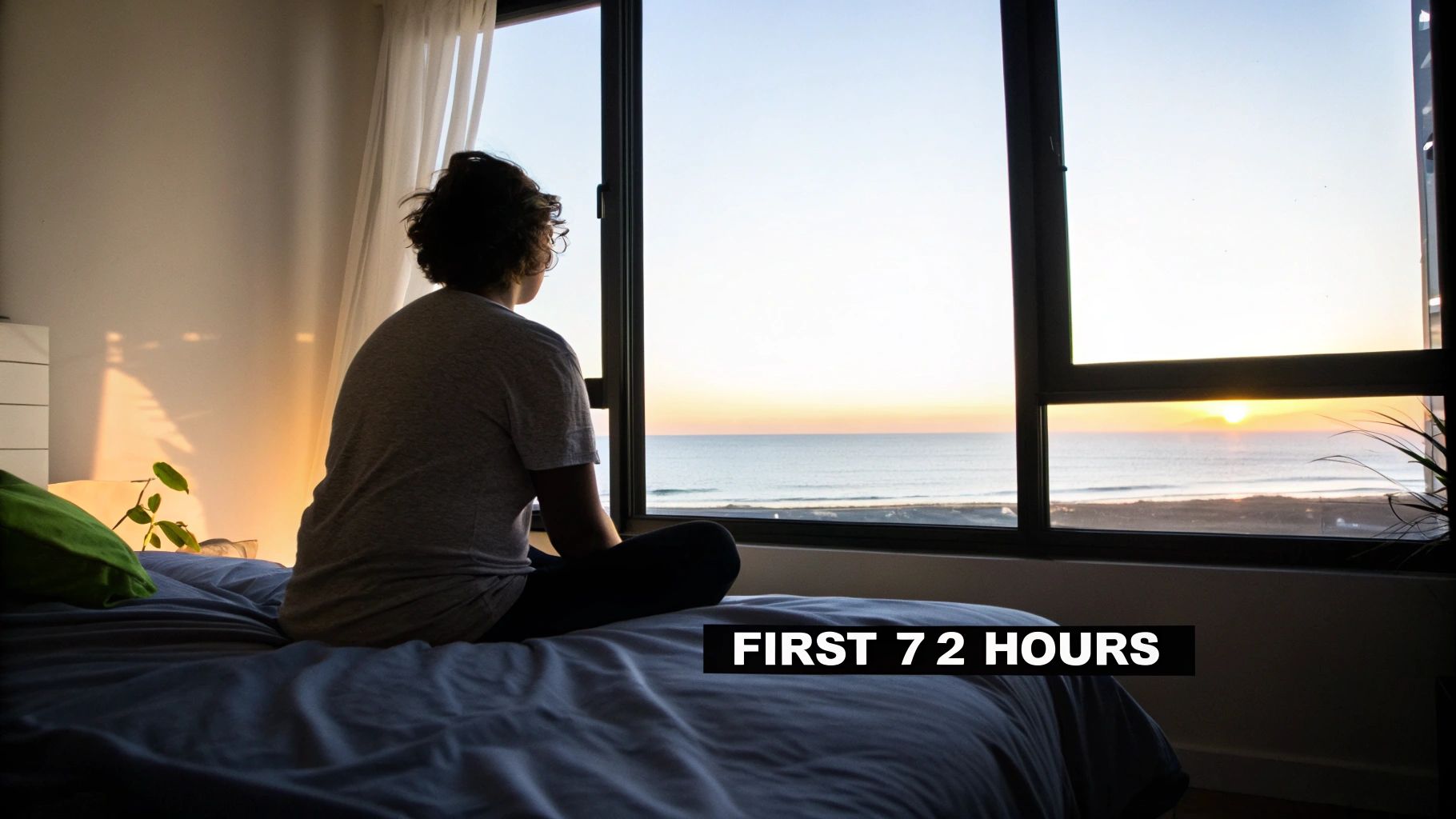 Person sitting on bed looking at ocean sunrise through window during early smoking withdrawal period