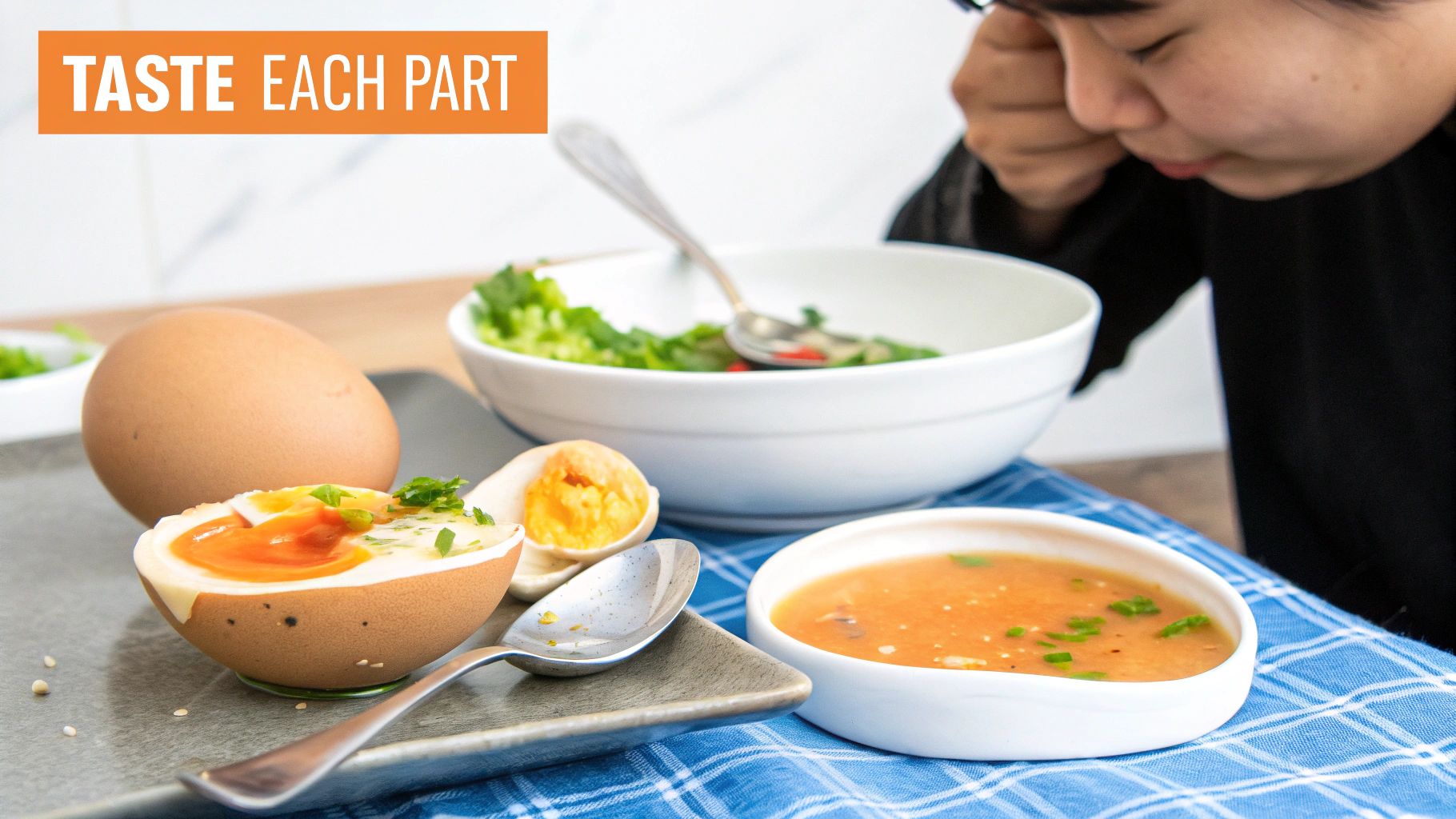 A person closely observes a soft-boiled egg, salad, and soup on a blue checkered table.