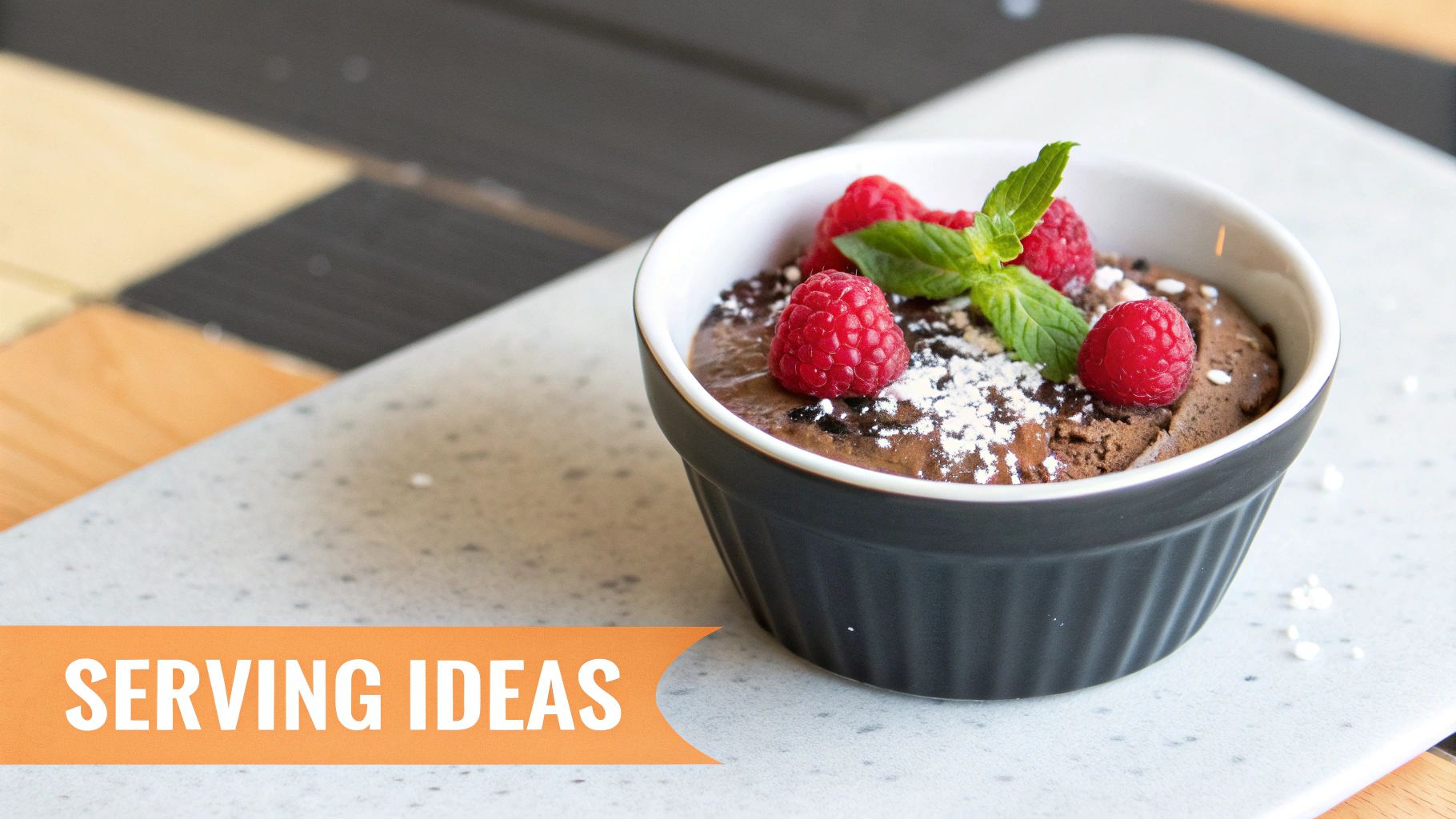 Rich dark chocolate mousse dessert in a black ramekin, garnished with fresh raspberries and mint.
