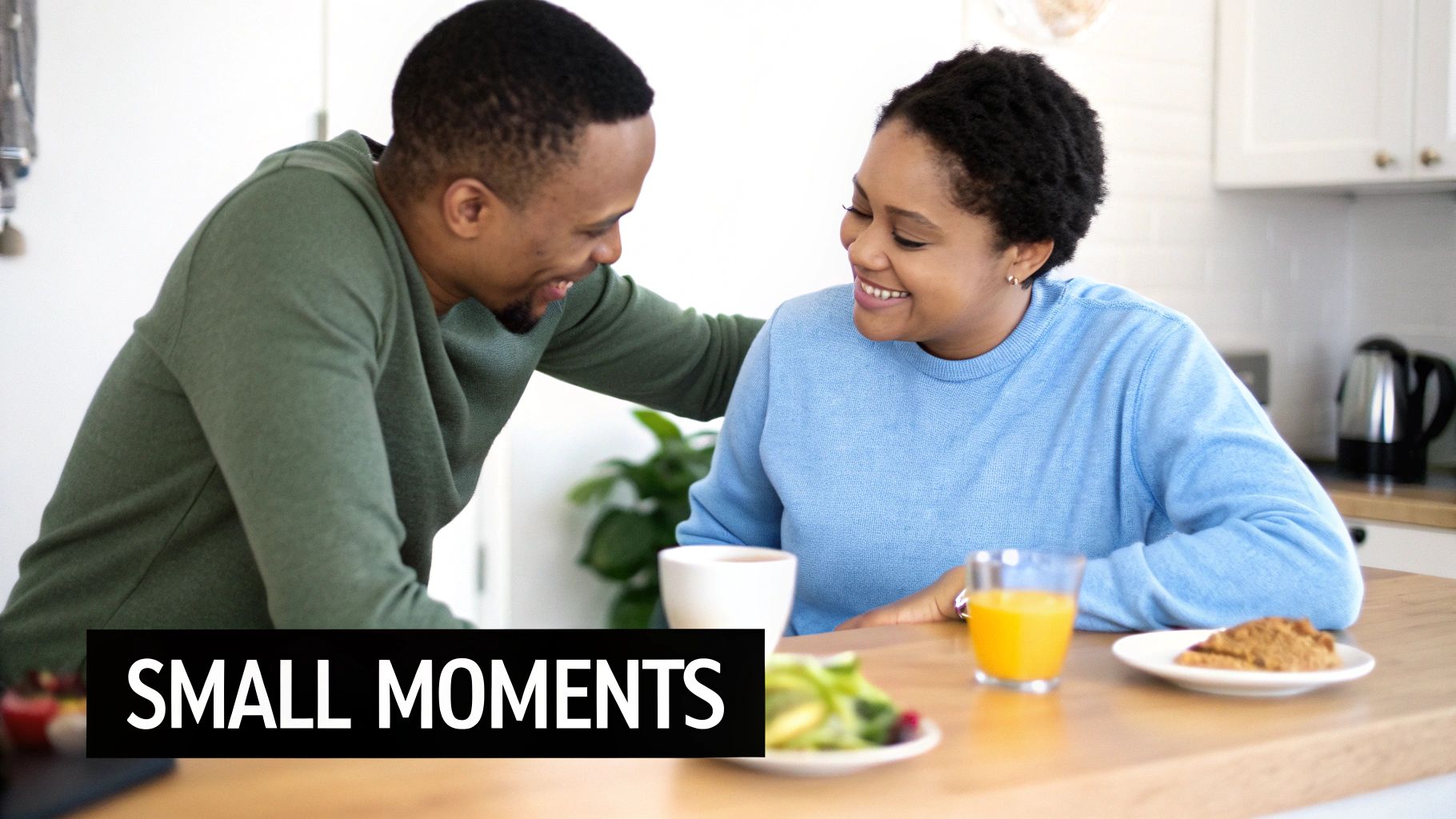 A smiling Black couple sharing a sweet moment over breakfast in a bright kitchen.