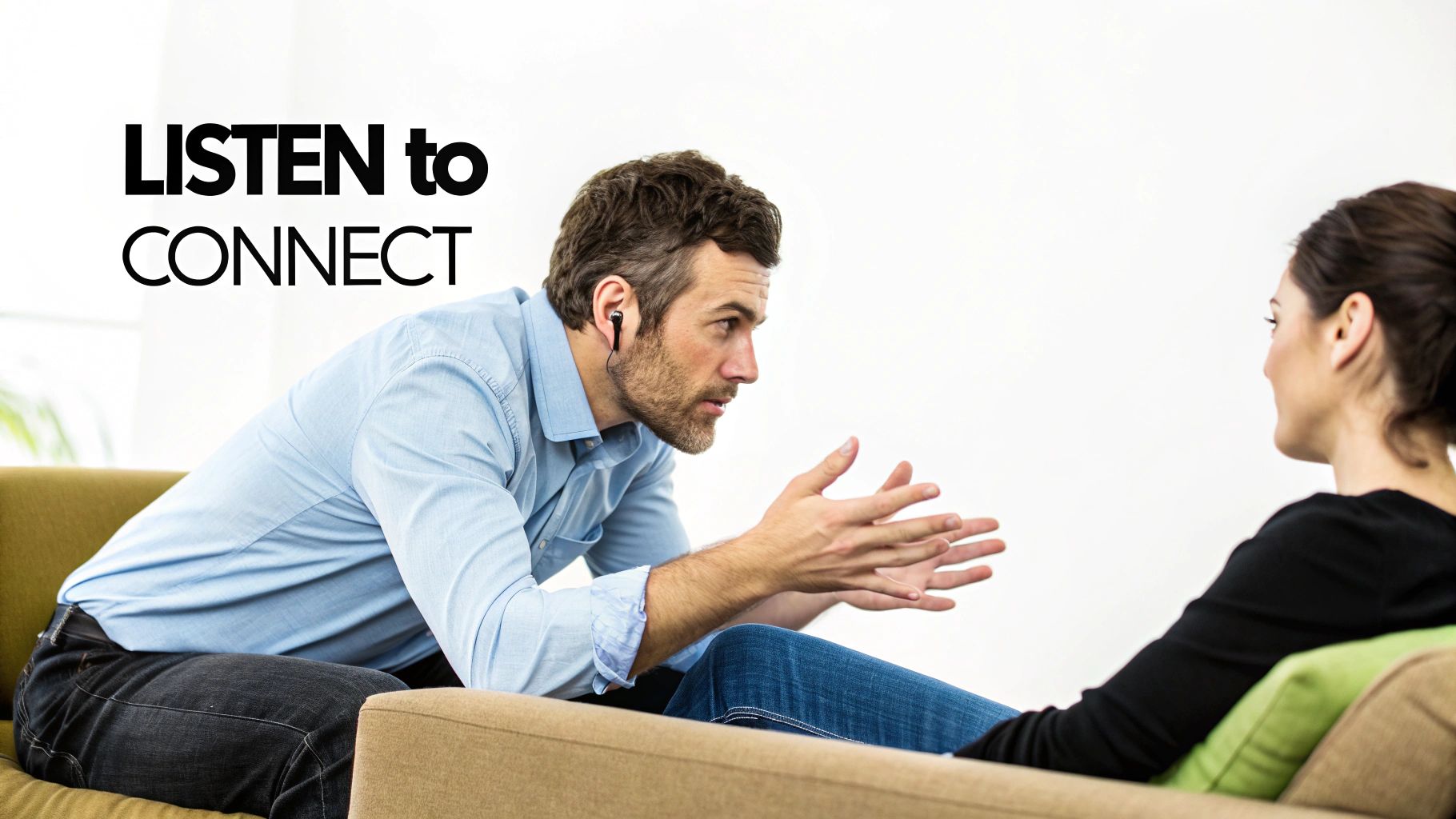 A man with an earbud actively listens and gestures while talking to a woman on a couch.