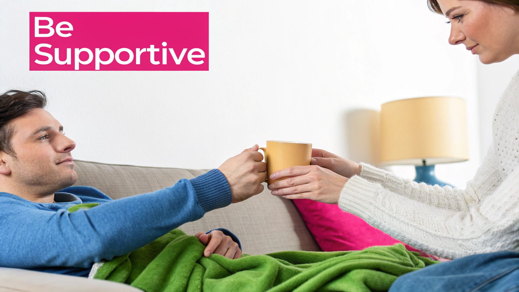 A woman gives a yellow mug to a man resting on a couch under a green blanket, illustrating support.
