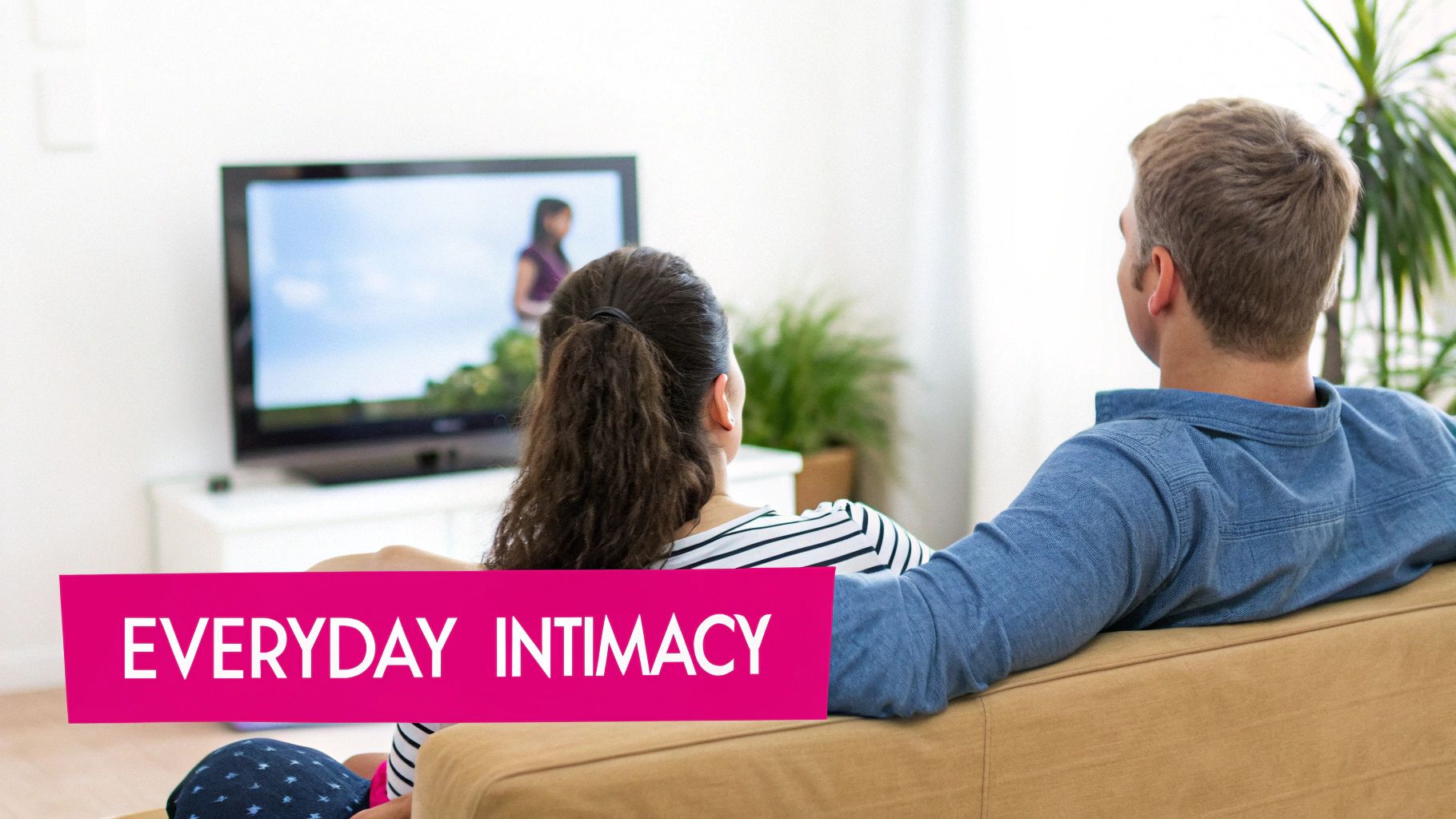 A couple from behind, sitting comfortably on a couch, watching television together.