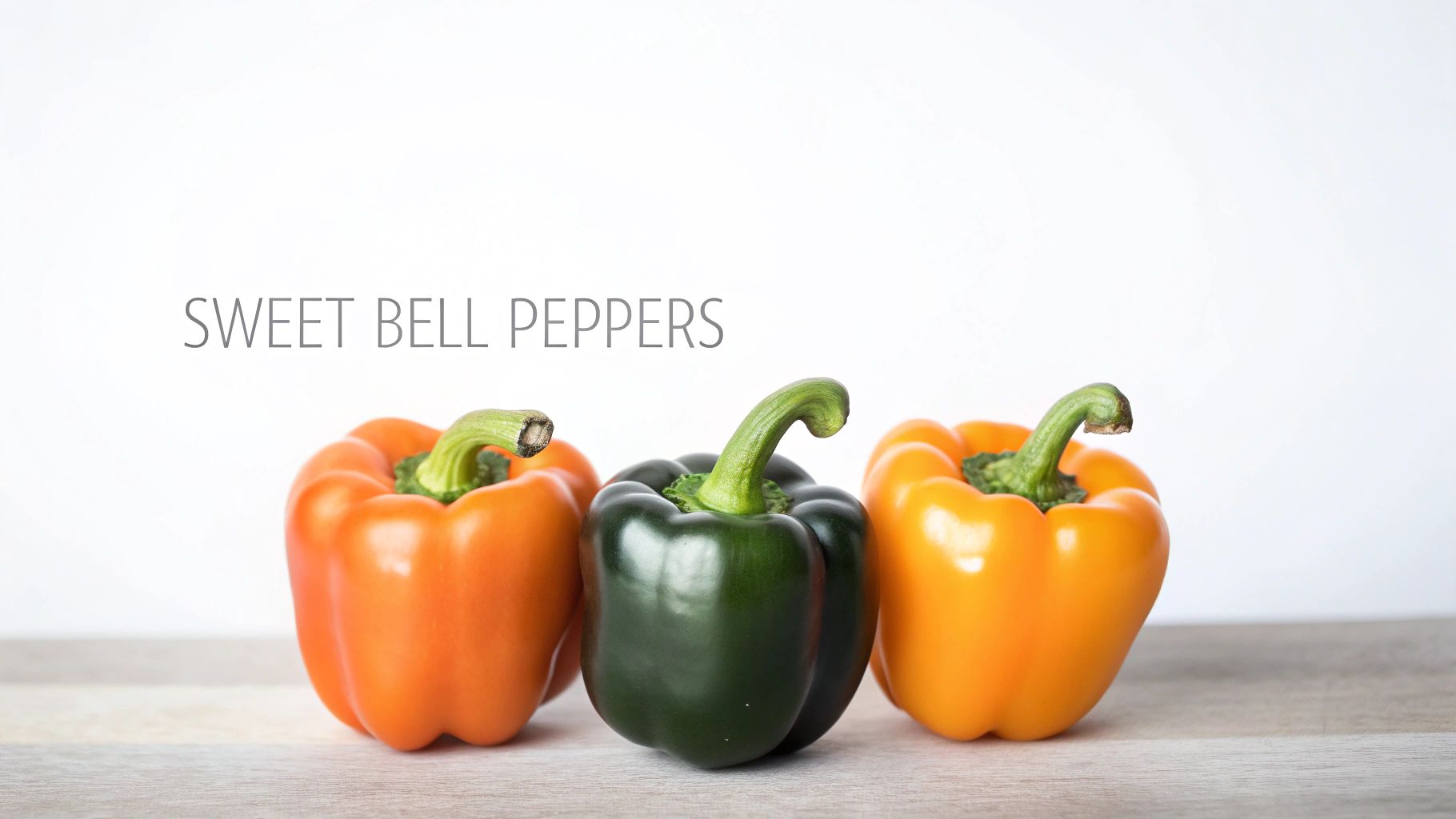 Three vibrant sweet bell peppers, including green and orange, displayed on a light wooden surface.