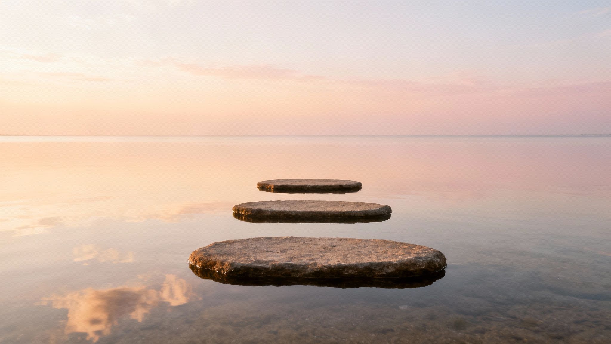Three stepping stones float on calm water towards a pastel sunset horizon.