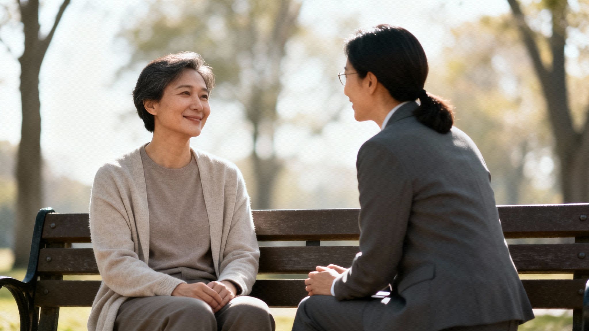 Two women, one older and one younger, sit on a park bench and talk.
