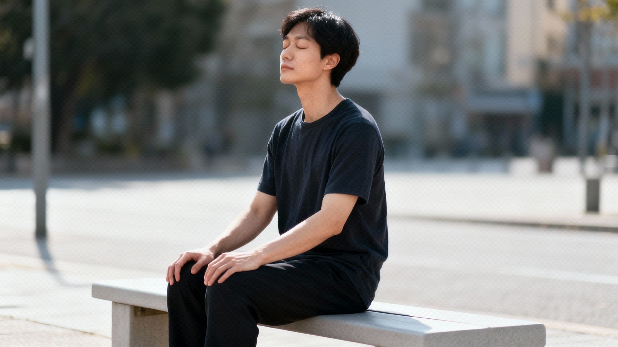 Asian man meditating with closed eyes on a park bench, finding peace outdoors.