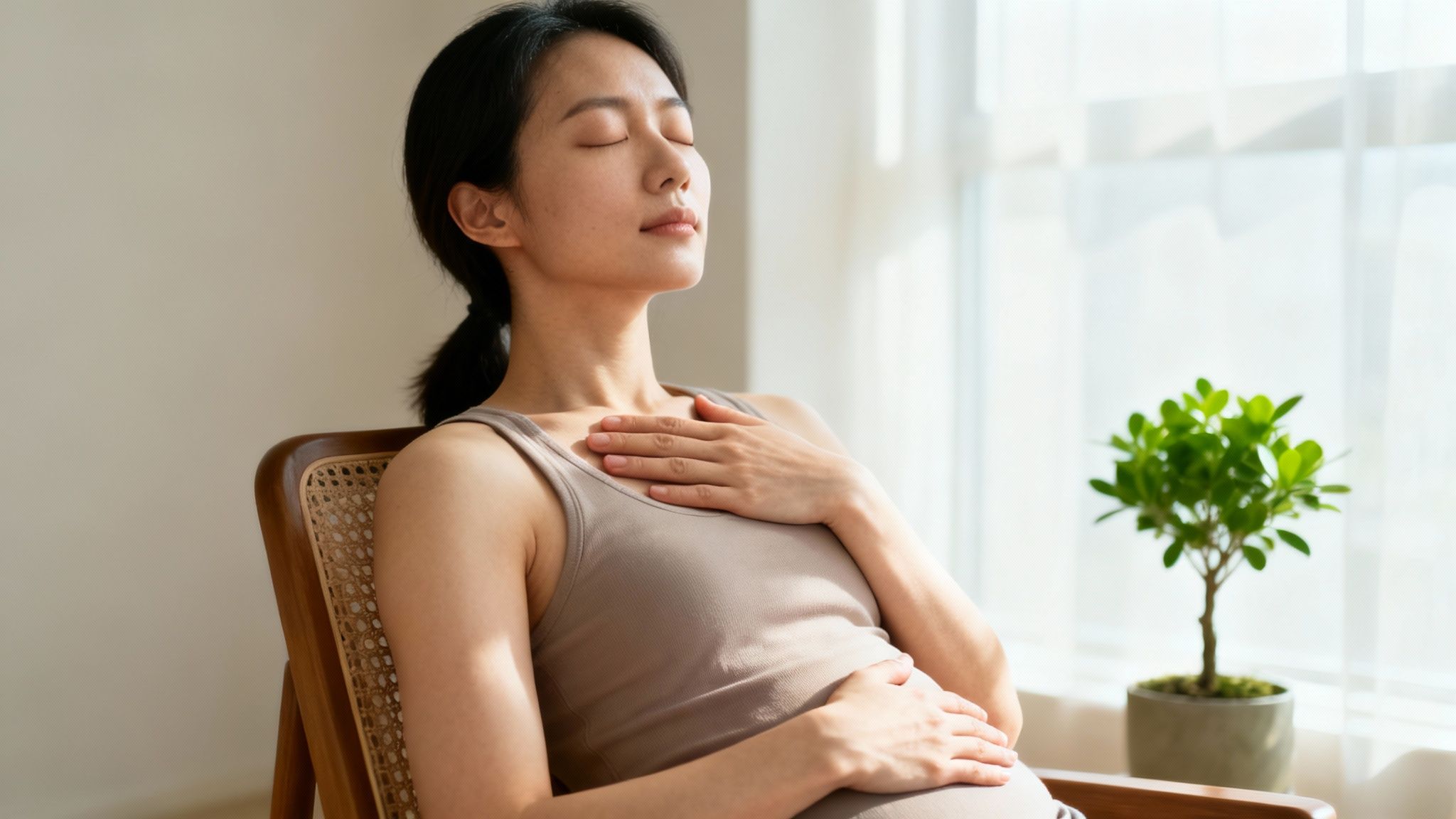 Peaceful Asian woman with closed eyes relaxing in a chair, hands on her chest and abdomen.