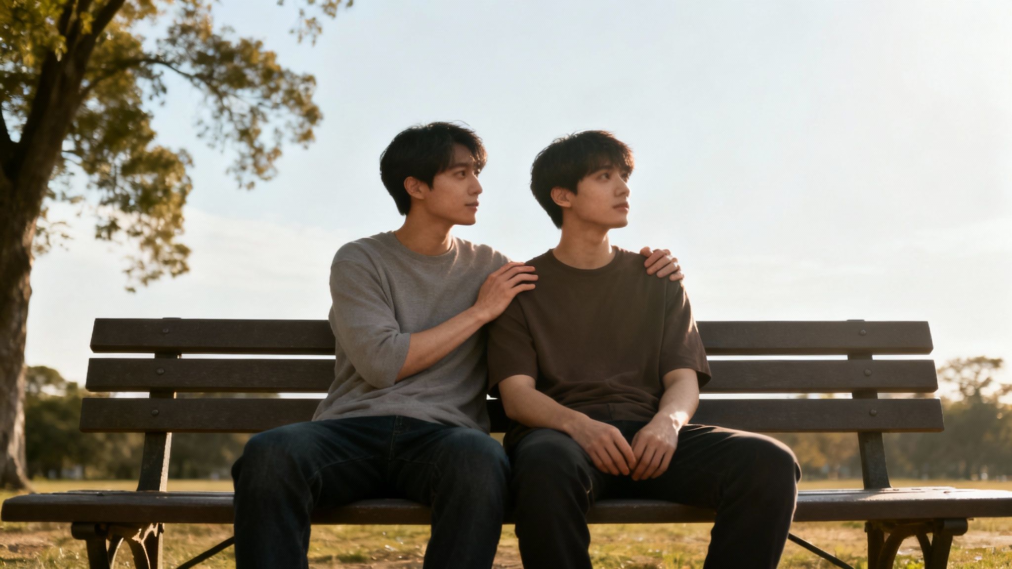 Two young men sitting on a park bench, one with a comforting hand on the other's shoulder.