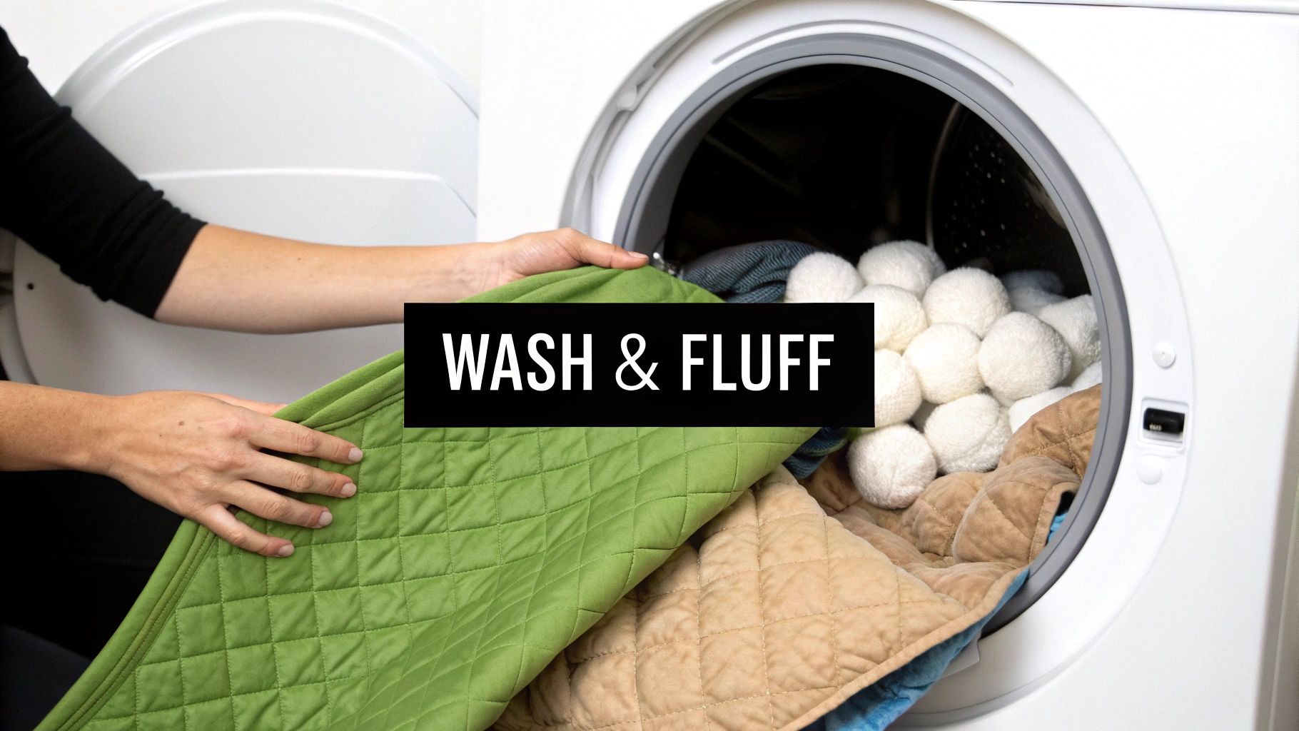 A person loads a green quilted blanket into a white front-load washing machine, which contains other blankets and dryer balls.