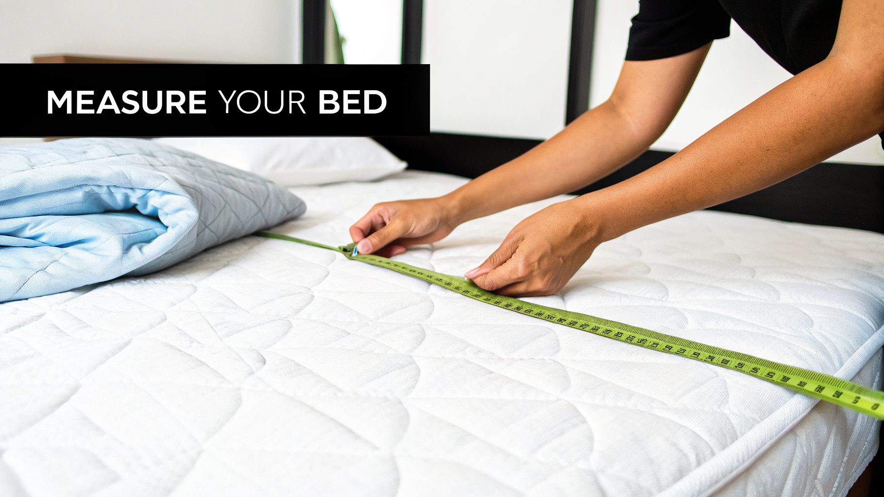 A person measures a white quilted mattress with a green tape measure, with a blue quilt nearby.