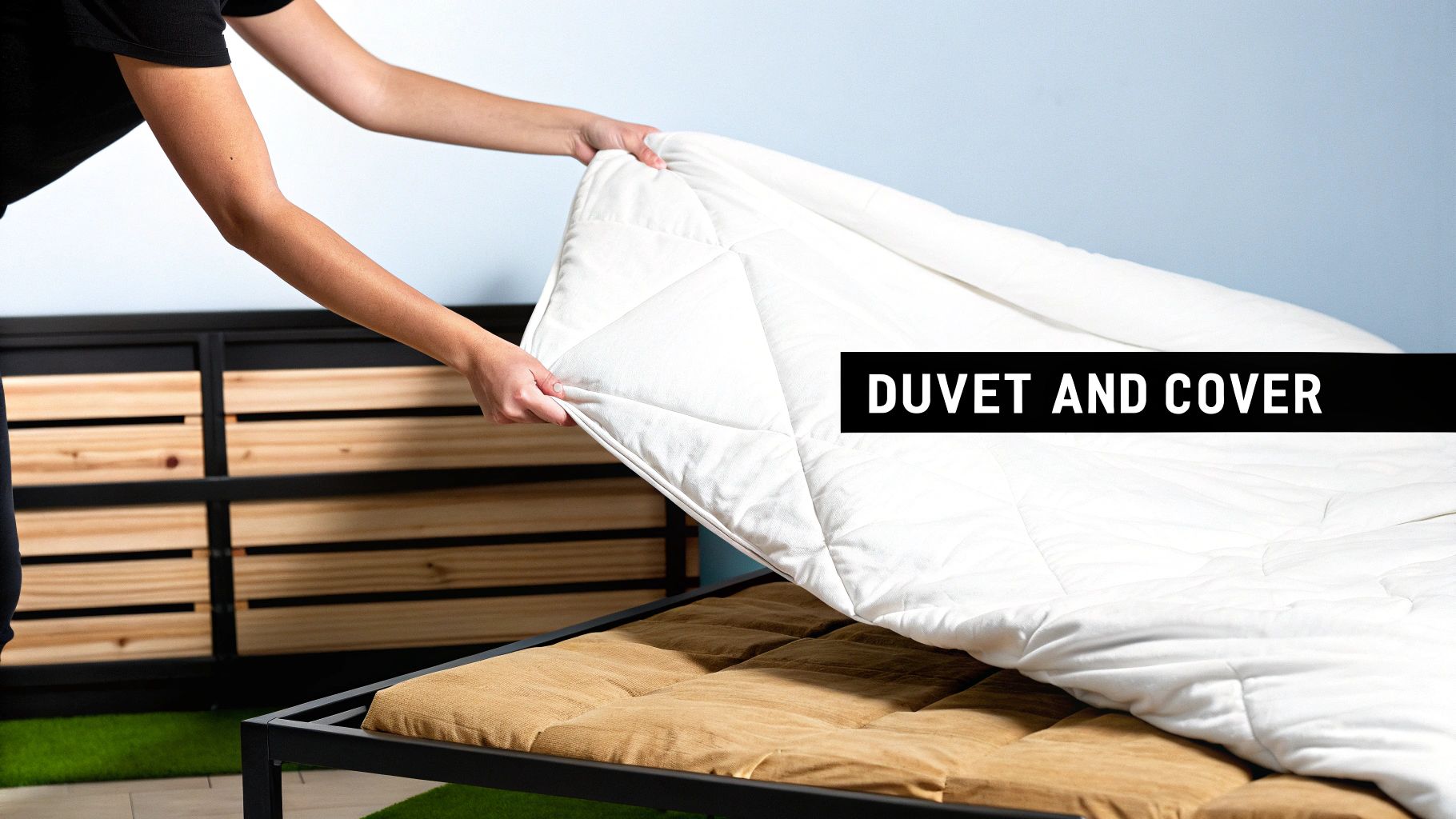 A person's arms are shown placing a white, quilted duvet onto a bed with a brown mattress.