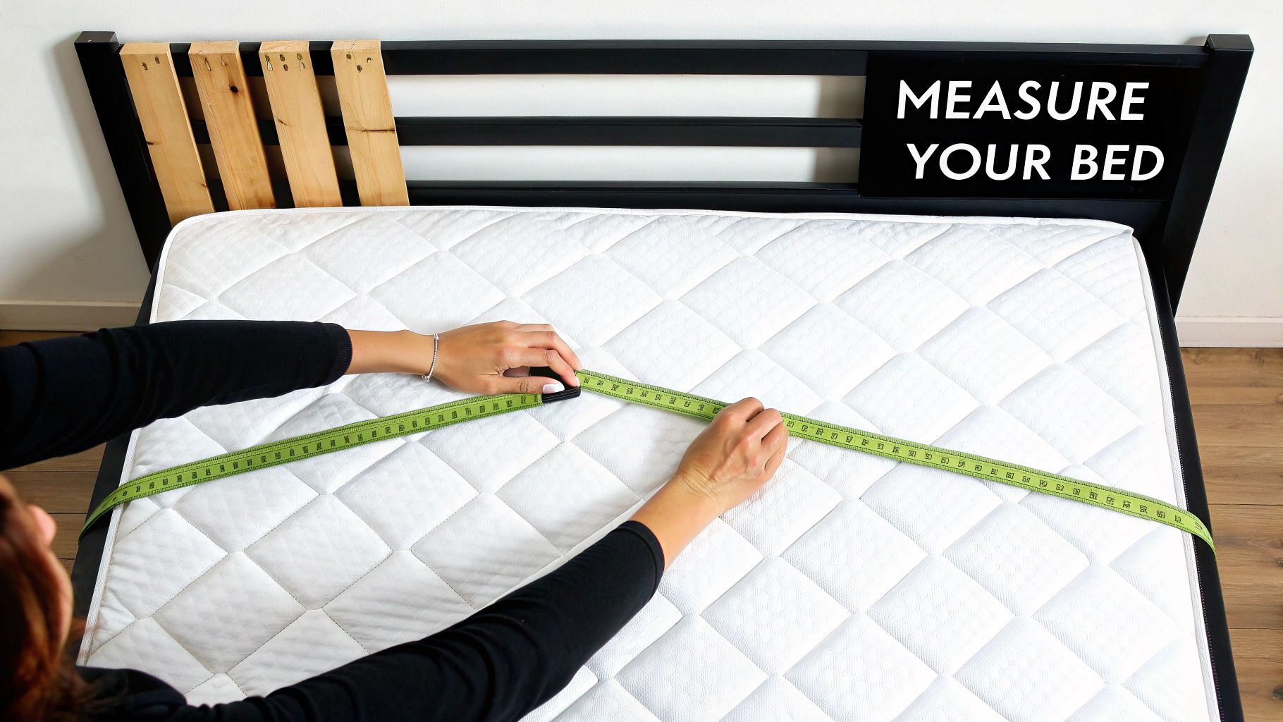 A person is measuring a white quilted mattress on a black bed frame with a green tape measure.