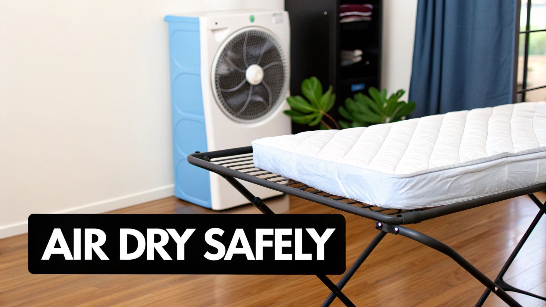 A white mattress topper air-drying on a black rack indoors, with a fan and plant in the background.