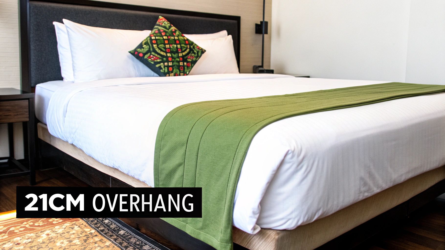 A neatly made double bed in a hotel room, featuring a white doona and green bed runner.