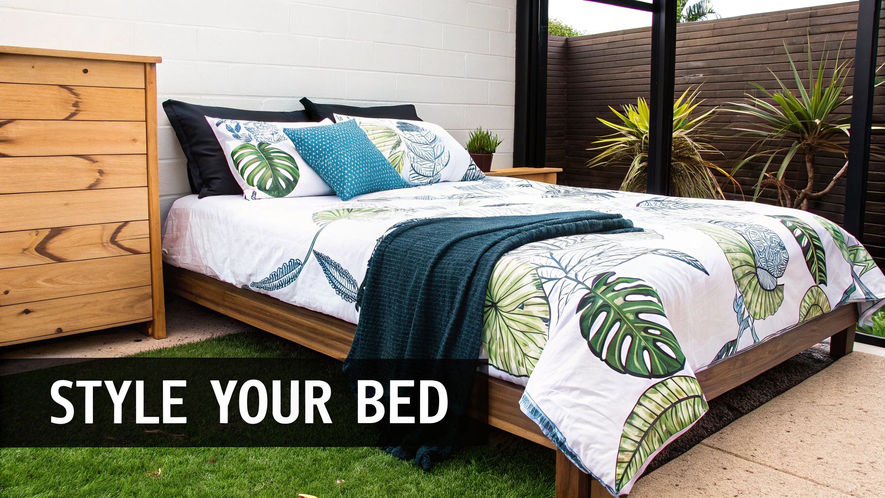 A beautifully styled bed with tropical leaf print duvet, teal throw, and accent pillow in a bright room.