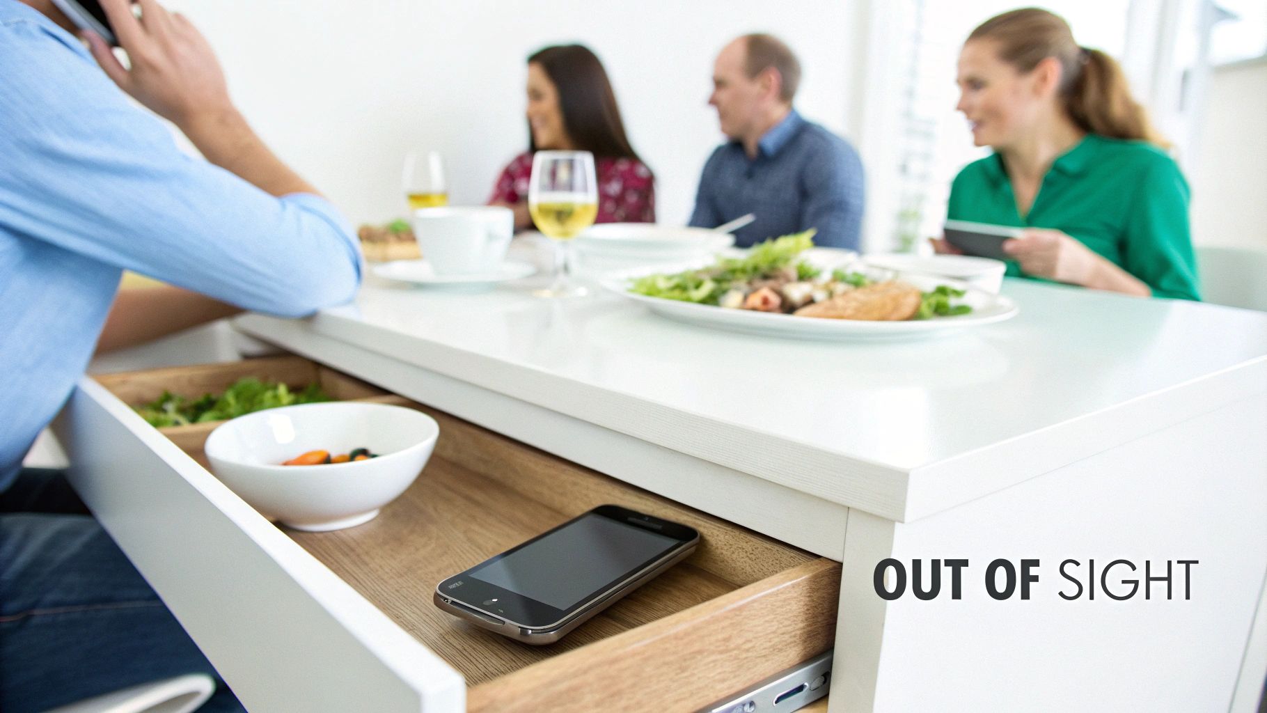 Smartphone placed on desk drawer while people enjoy meal together at dining table