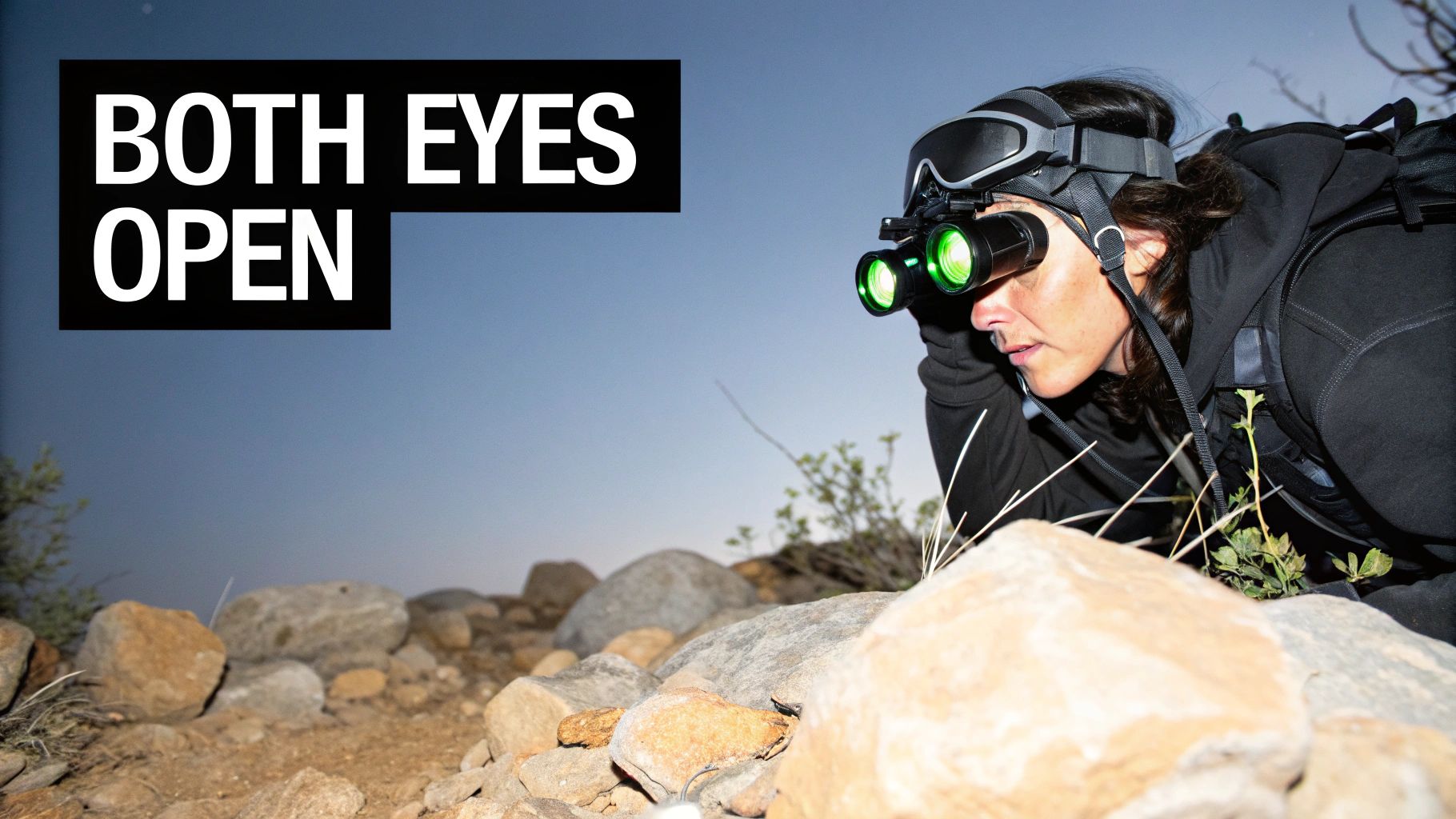 A woman wearing binocular night vision goggles observes rocky terrain at night.