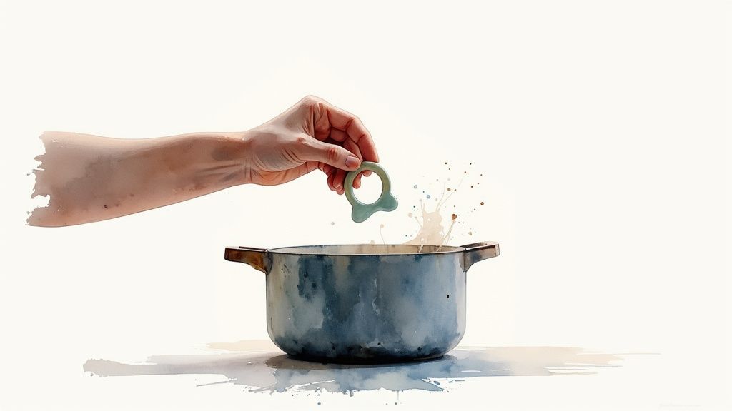 A hand holds a green, ring-shaped baby teether above a blue pot with playful splashes.