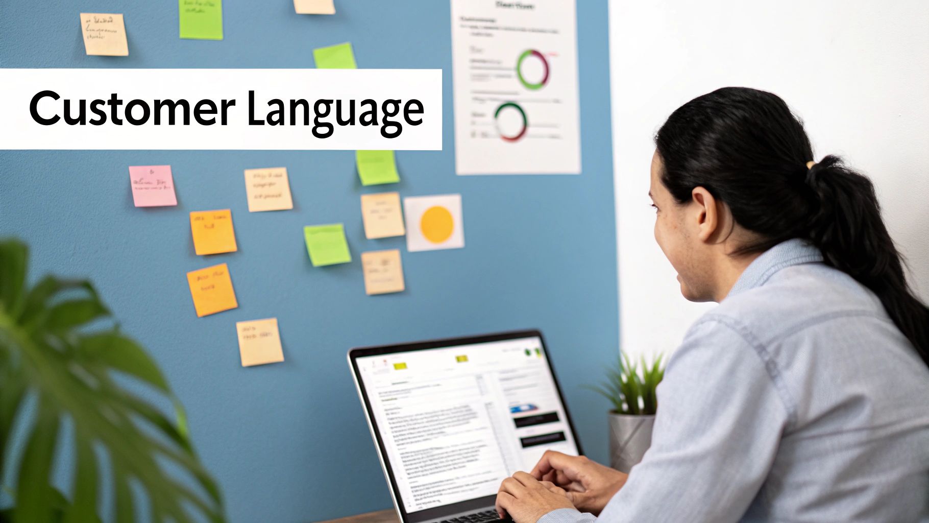 A person typing on a laptop with "Customer Language" text and sticky notes on a blue wall.