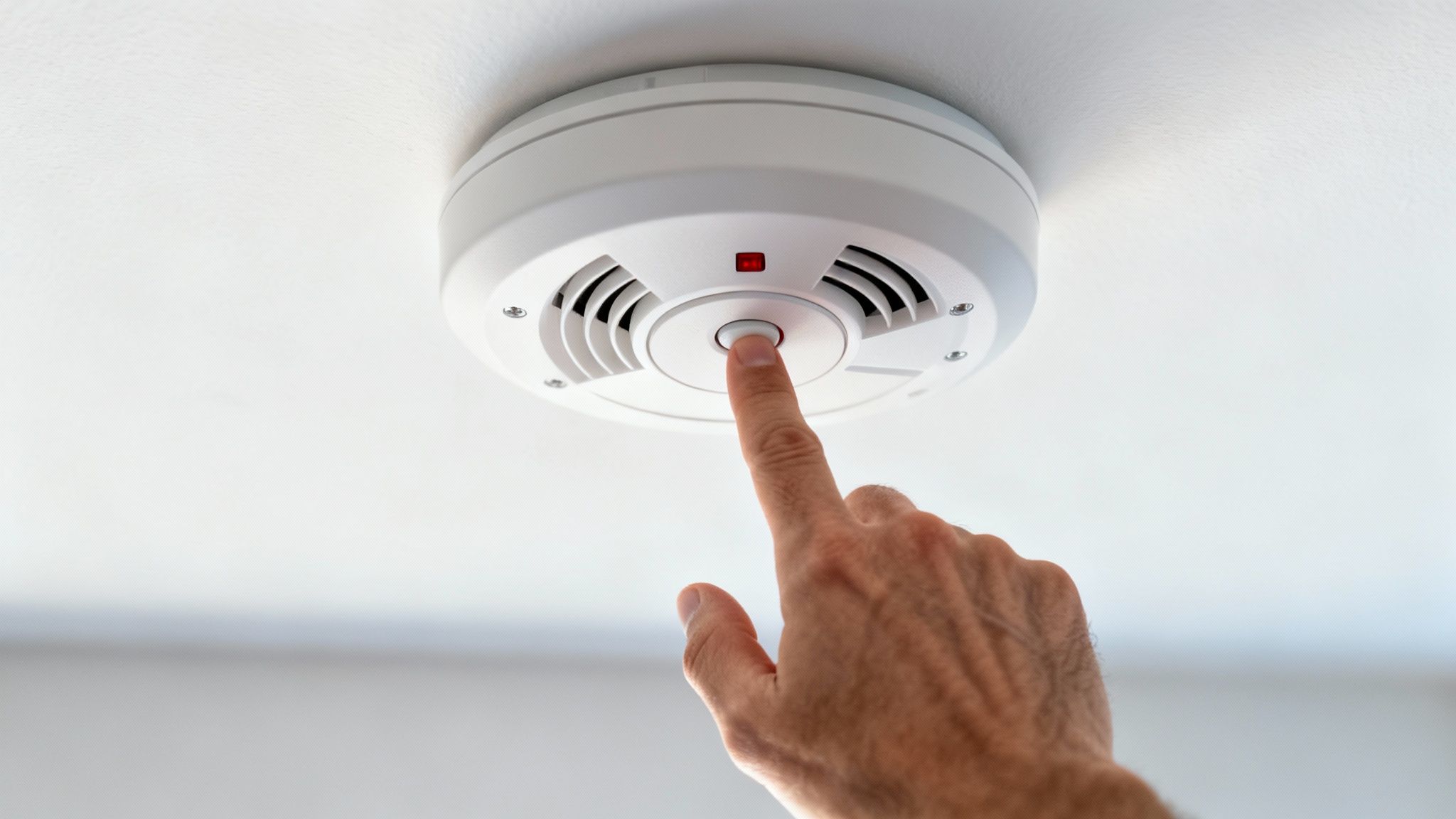 A Person Testing A Smoke Alarm On The Ceiling With A Broom Handle.