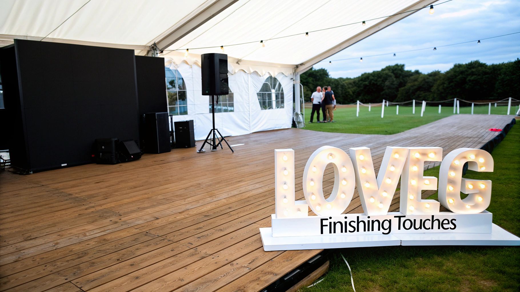 Elegant white wedding marquee with wooden floor, event equipment, and a prominent lighted 'LOVE' sign.