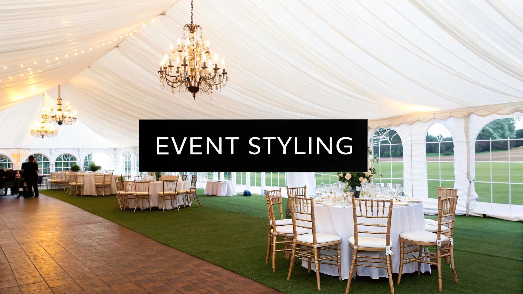 An elegant white marquee tent interior, featuring round tables, gold chairs, and ornate chandeliers for an event.