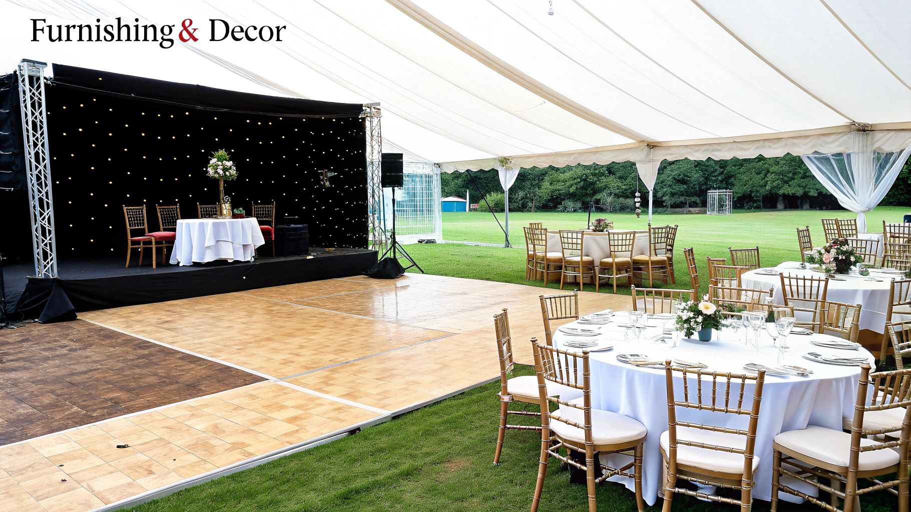 A large white marquee tent prepared for a wedding reception, featuring a stage and dining tables.