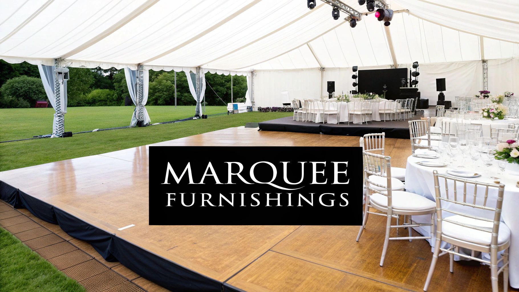 An elegant white marquee tent set up for an outdoor event, featuring dining tables, a dance floor, and stage.