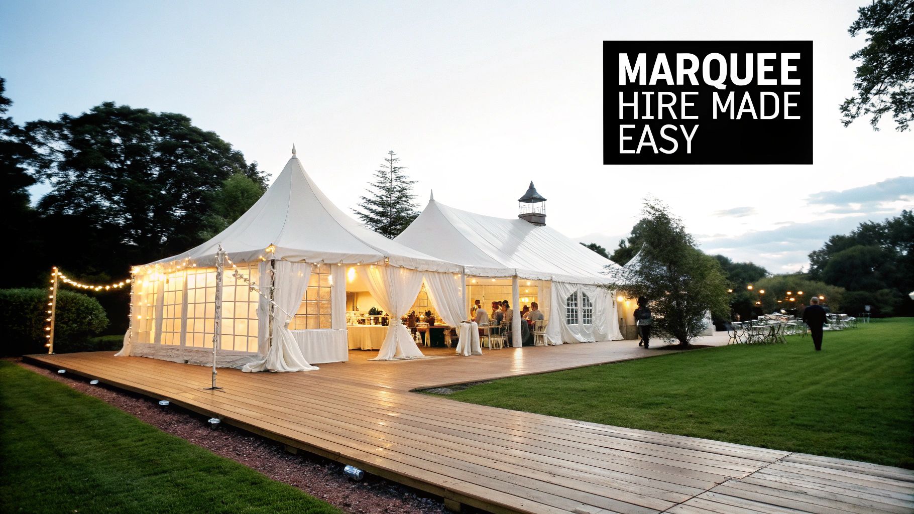 A large, beautifully lit white marquee tent on a wooden deck, ready for a wedding or event, with guests inside.