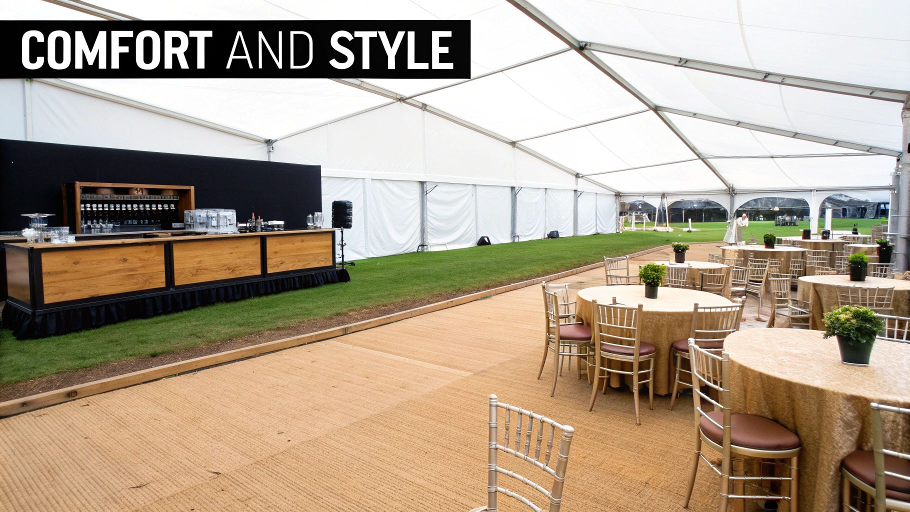 A stylish event marquee interior with a wooden bar, green grass, and gold-draped tables.
