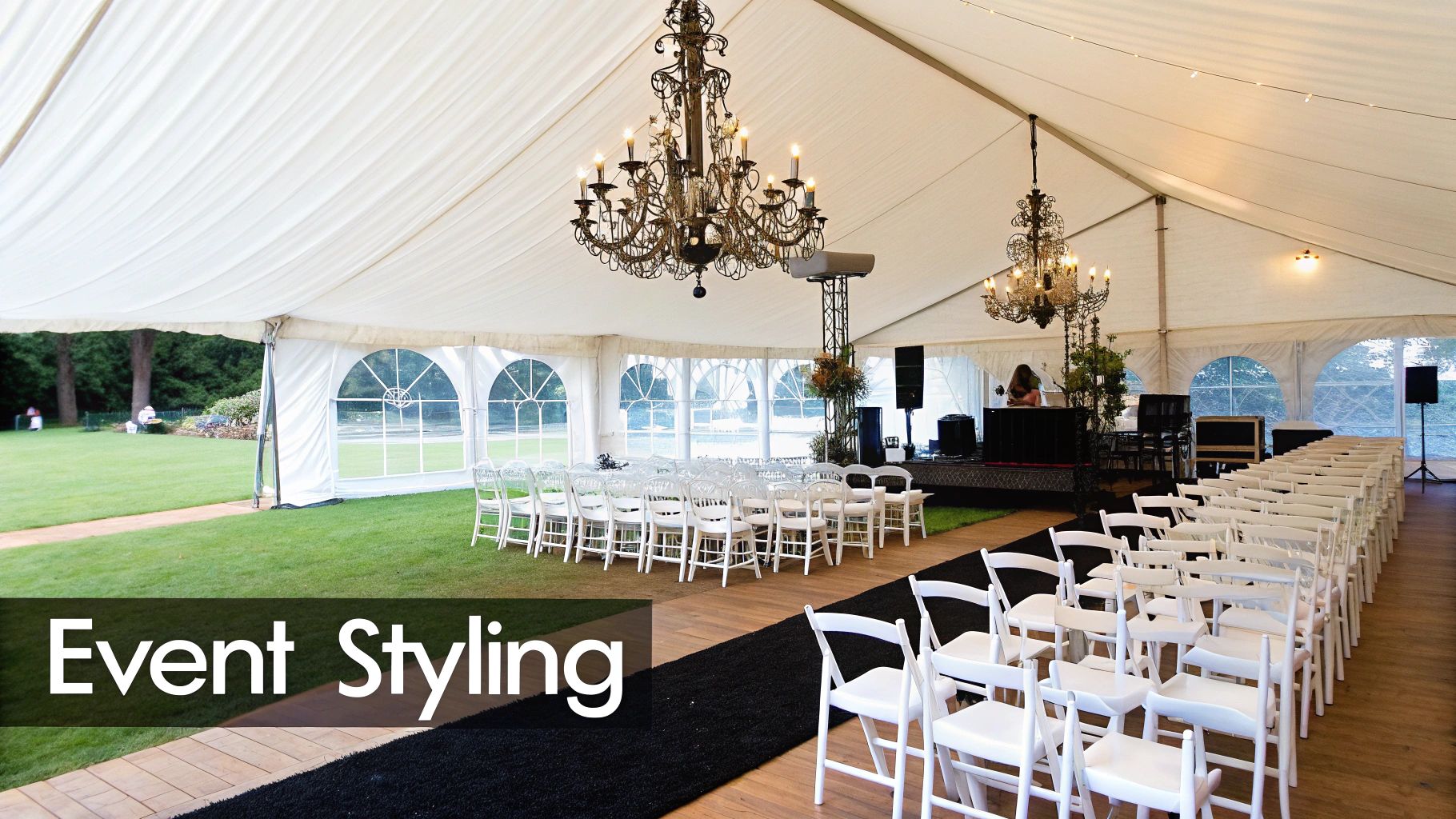 Inside a spacious white event tent with rows of white chairs, chandeliers, and a stage.