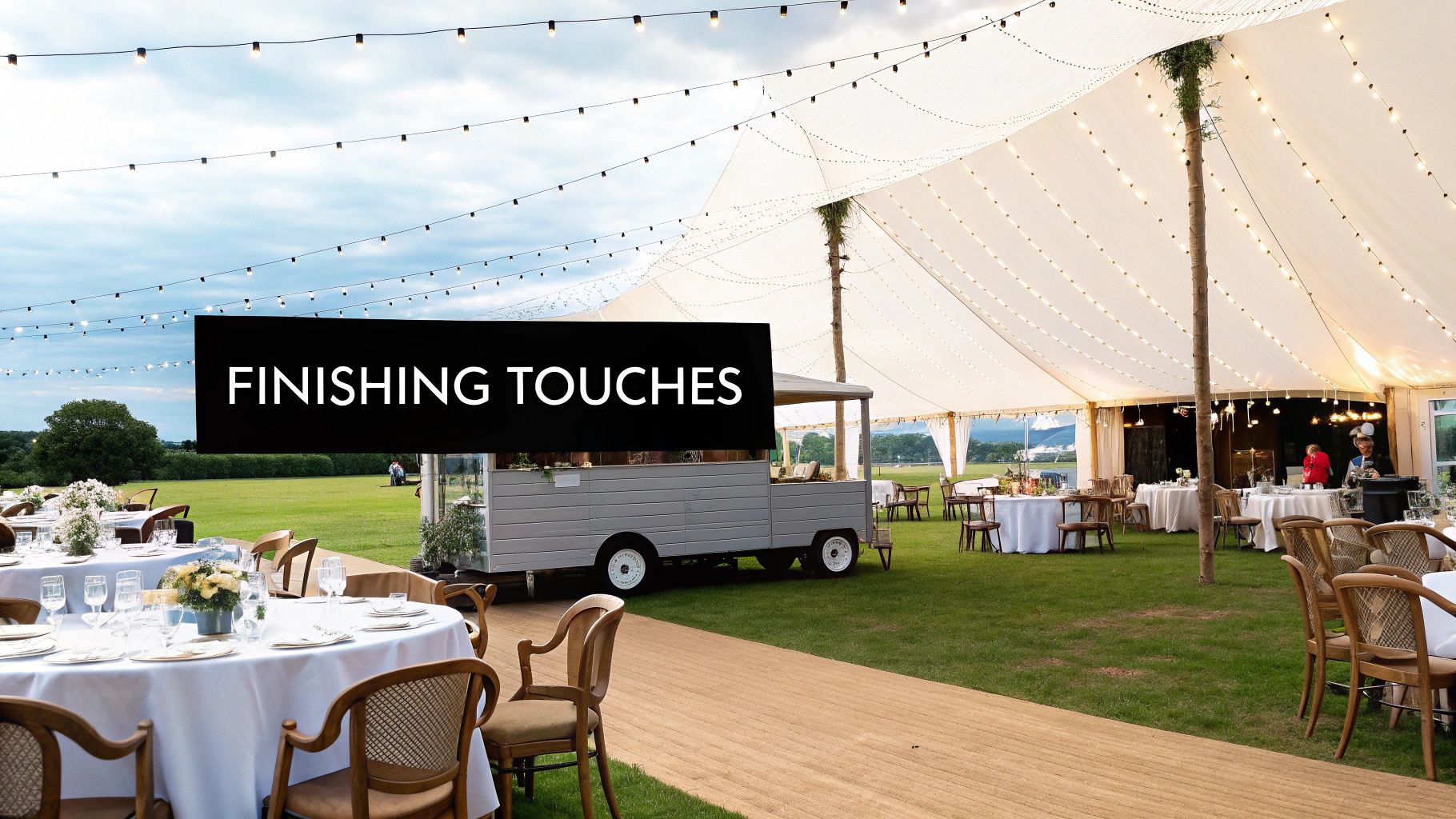 A beautifully decorated outdoor marquee event with fairy lights, elegant tables, chairs, and a mobile bar.