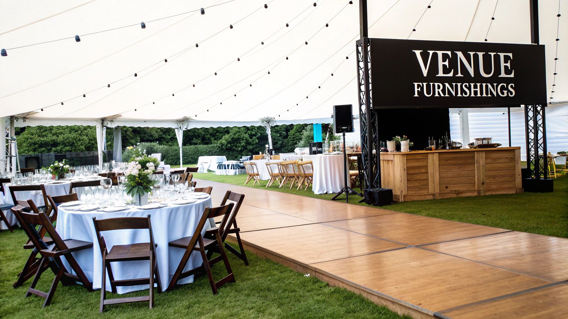 Elegant outdoor event setup under a white marquee tent with dining tables, chairs, a bar, and wooden pathway.