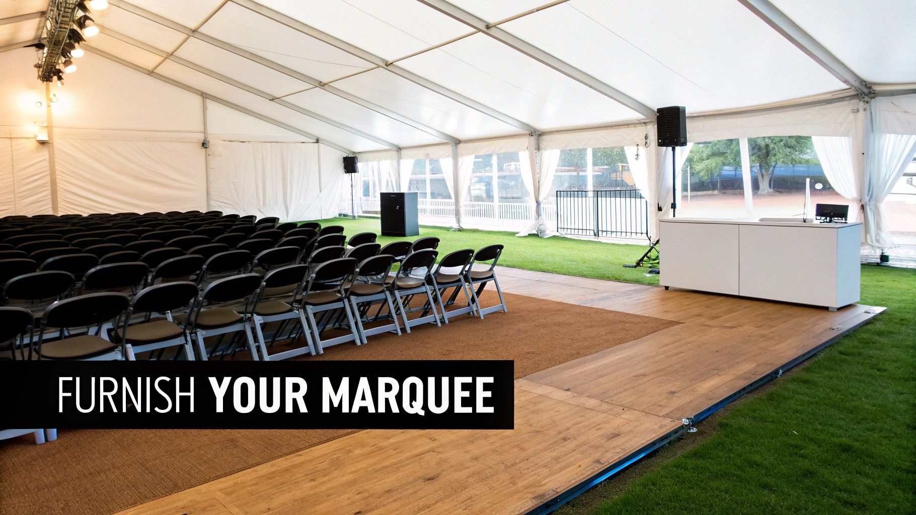 Interior of a white marquee tent with rows of black chairs, a wooden floor, and a white reception desk setup.