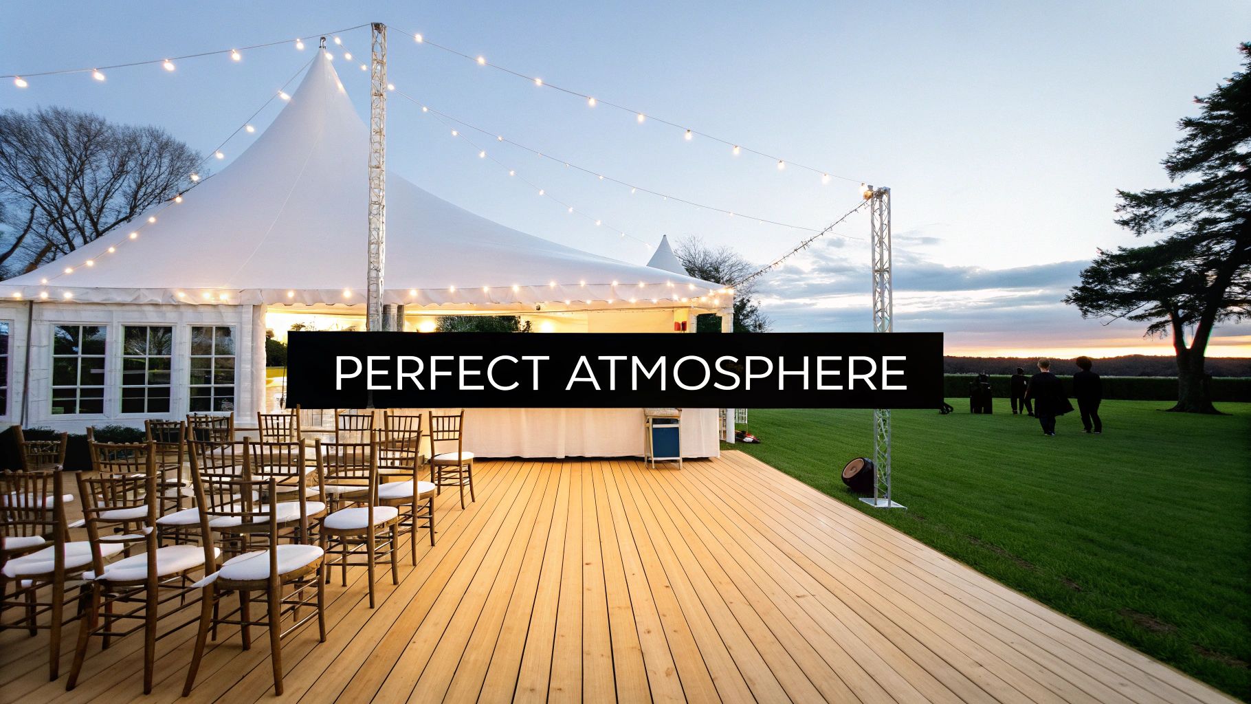 A beautiful white event marquee with string lights, a wooden deck, and chairs set up at sunset.