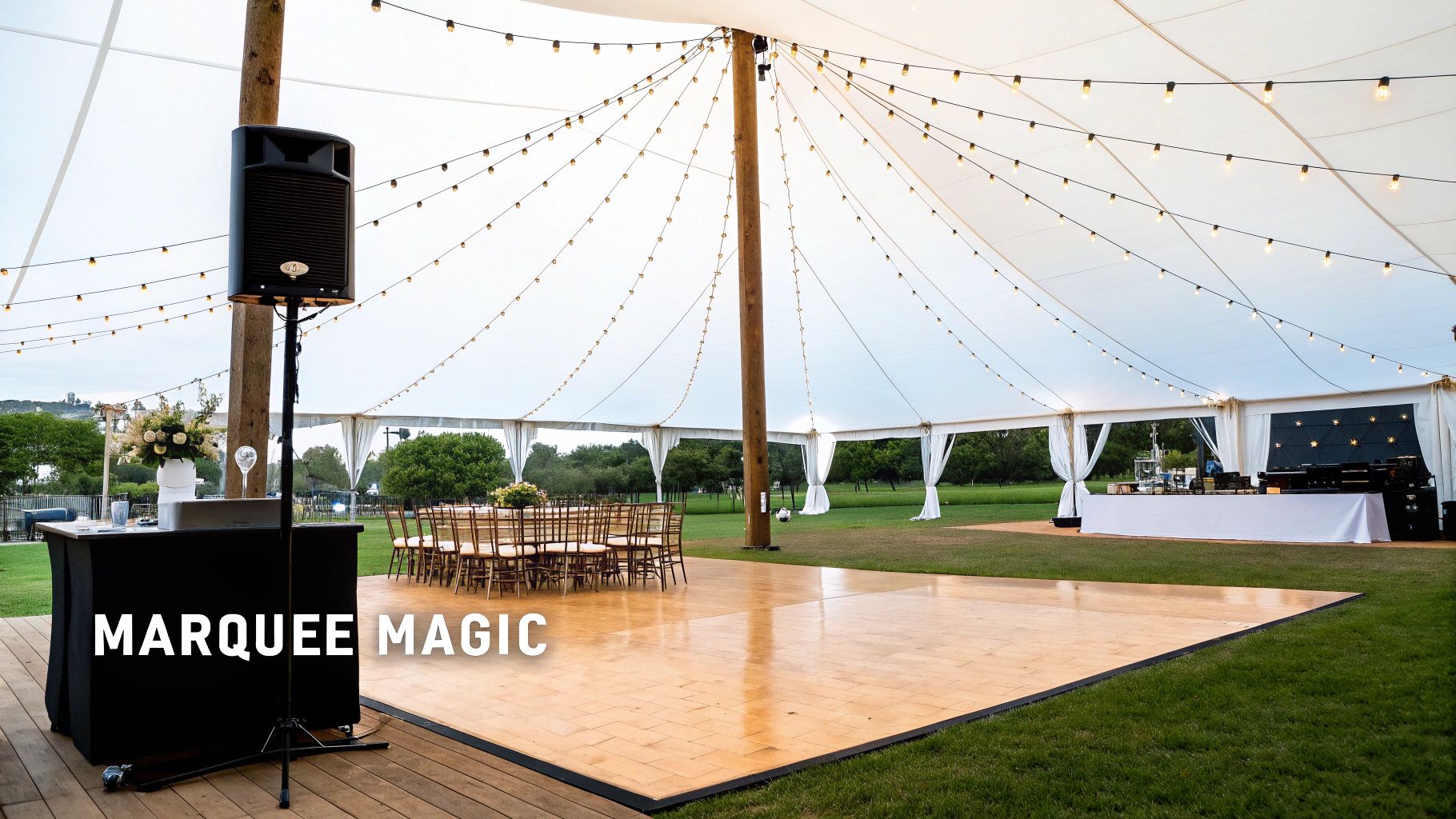 A spacious white marquee tent set up for an outdoor party, featuring a dance floor, tables, and string lights.