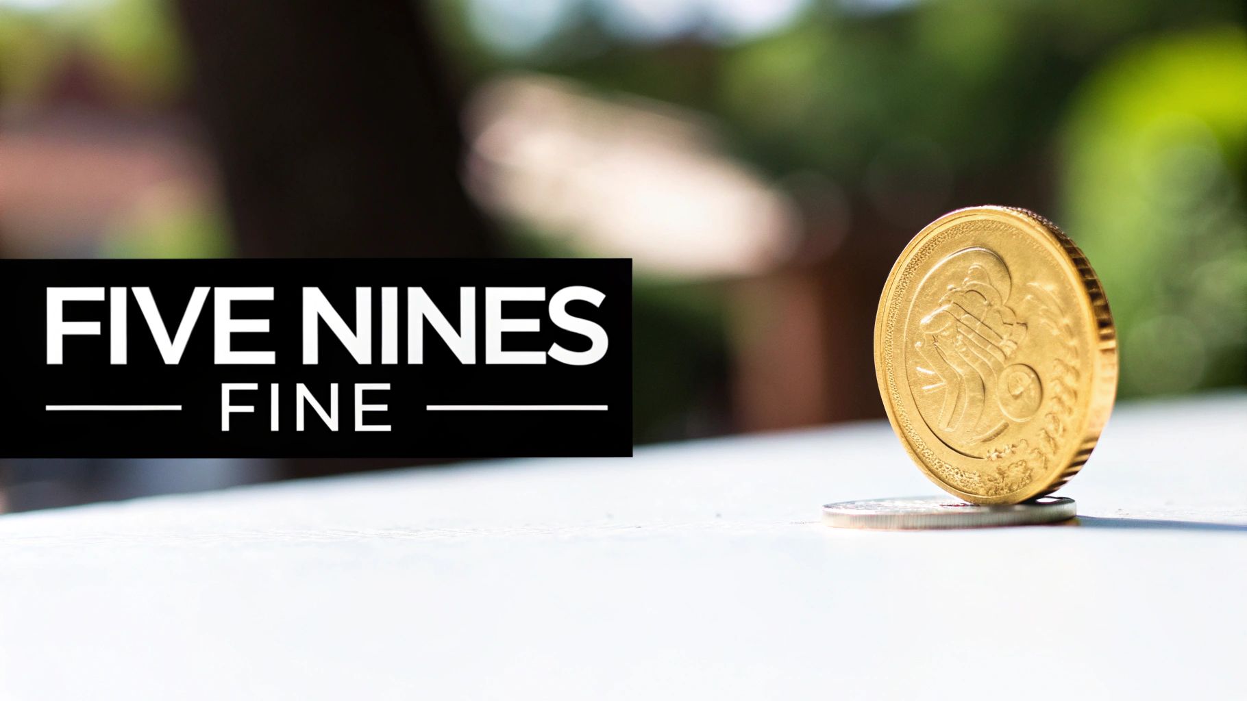 A golden coin stands on a silver coin beside a black sign displaying 'FIVE NINES FINE'.