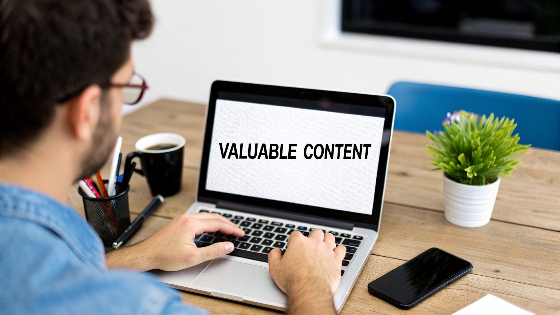 Over-the-shoulder view of a person typing on a laptop, displaying 'VALUABLE CONTENT', with coffee and a plant on the desk.