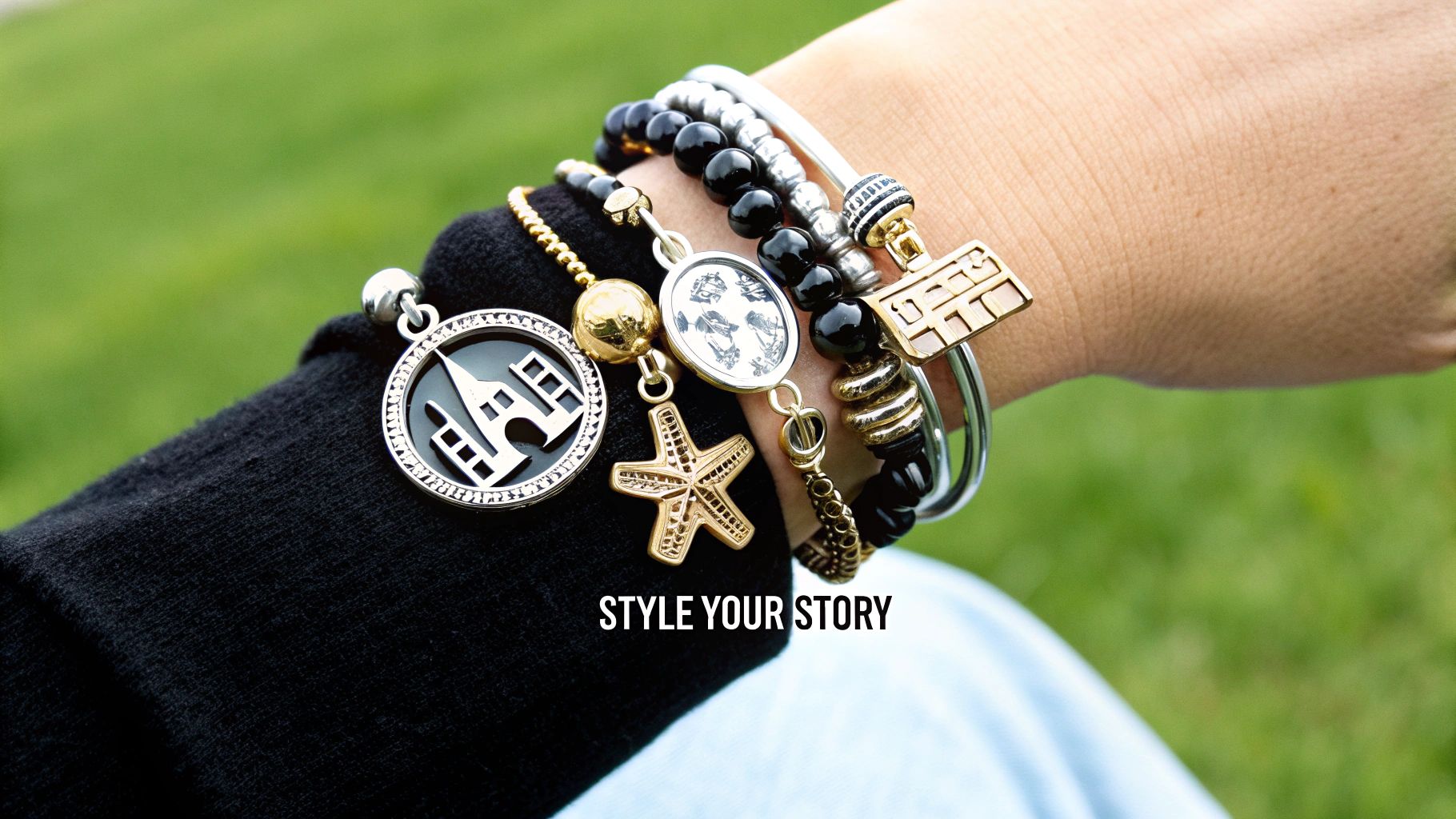 A person's wrist styled with multiple charm bracelets featuring castle, starfish, and bead charms outdoors.