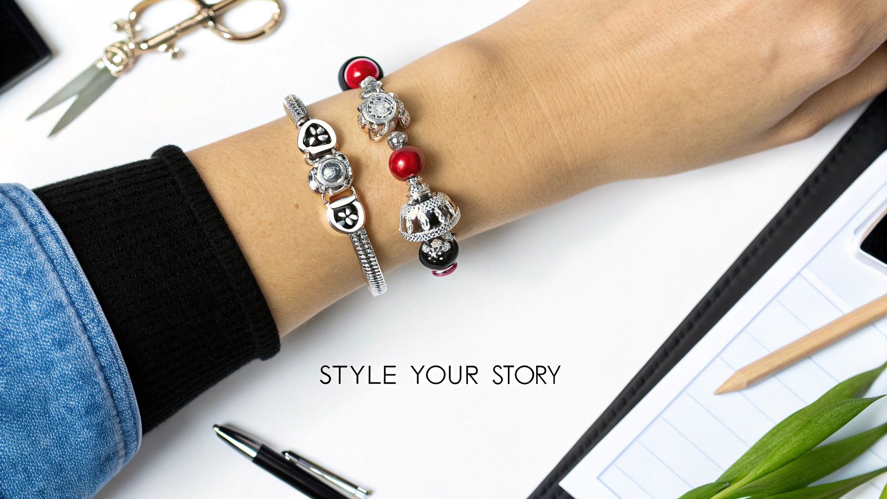 Close-up of a person's arm wearing two decorative charm bracelets on a white desk with stationery.