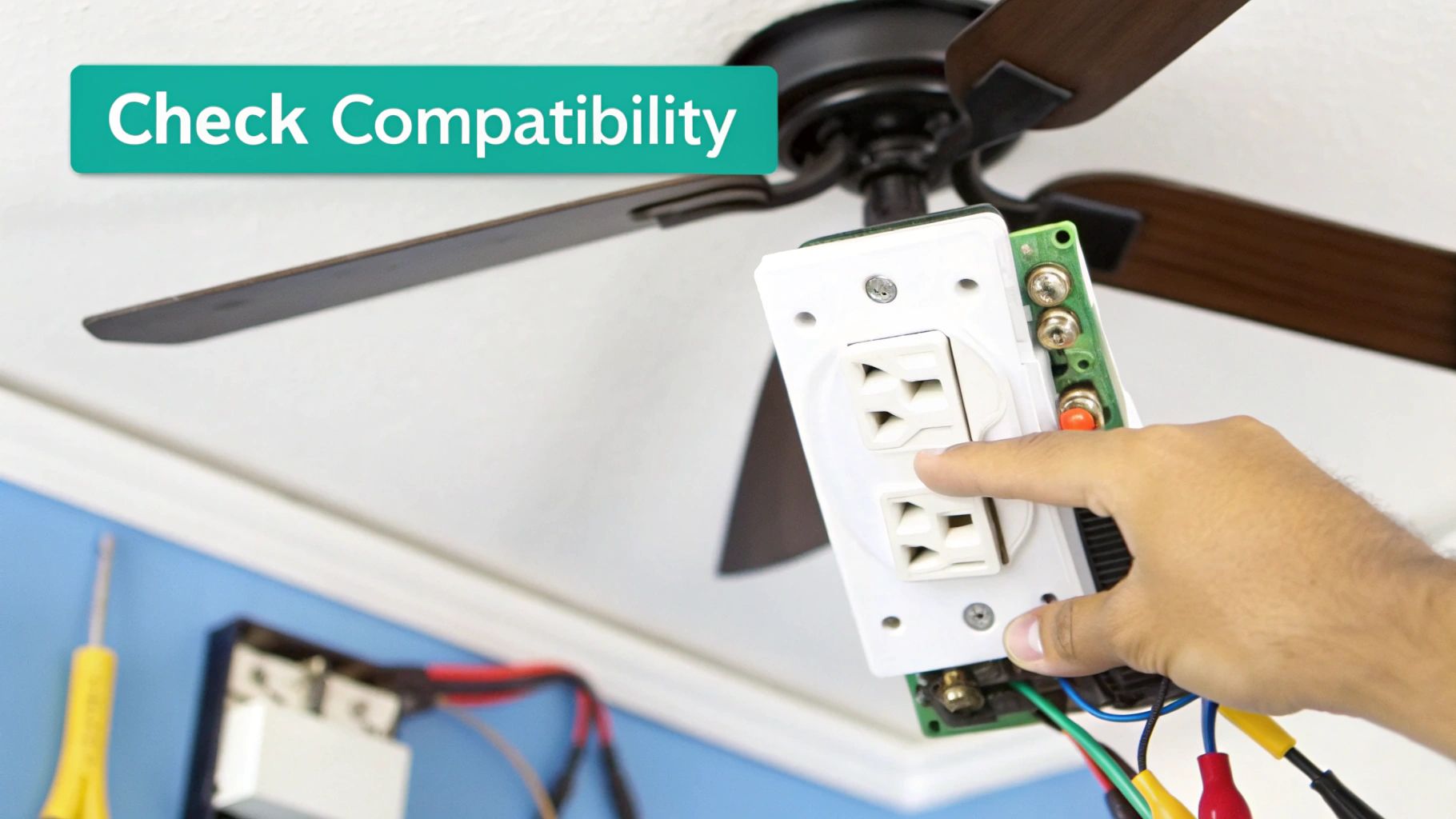 A hand holds an electrical outlet device with wires near a ceiling fan while checking compatibility.