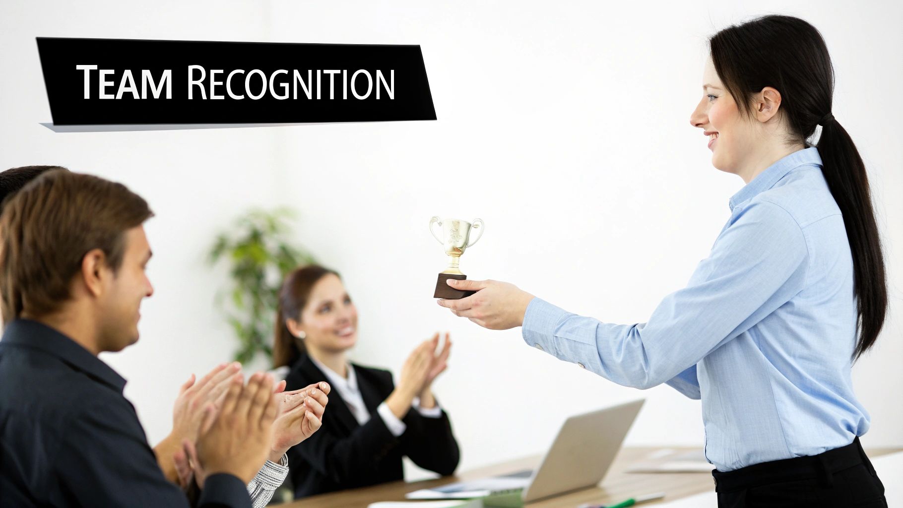 A smiling woman presents a golden trophy to a colleague, while team members applaud during a recognition event.