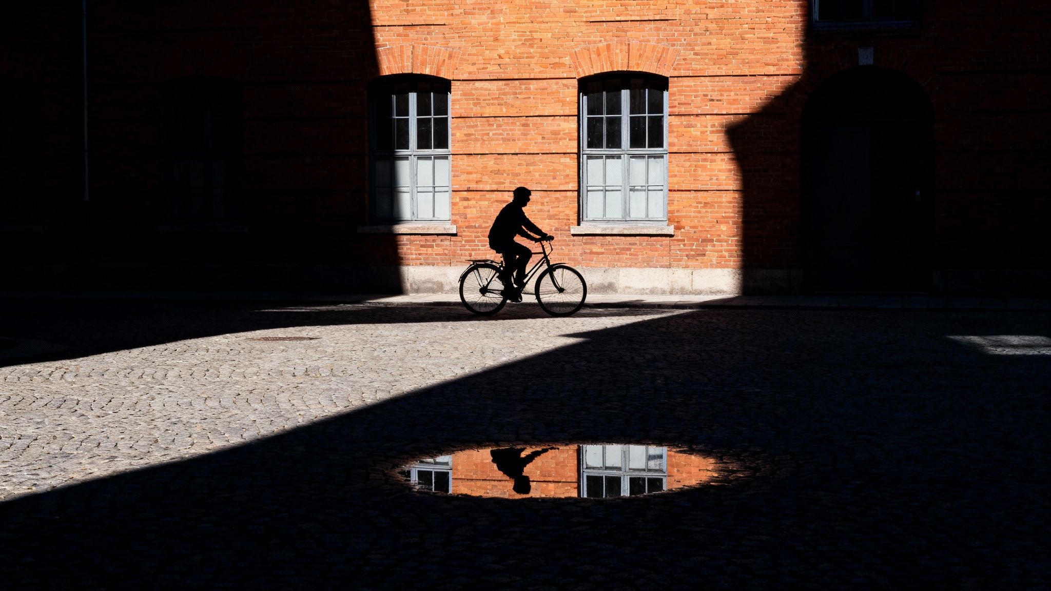 best photo locations near me: top spots for your shoot 4 A cyclist silhouetted against a sunlit brick wall with windows, reflected in a ground puddle.
