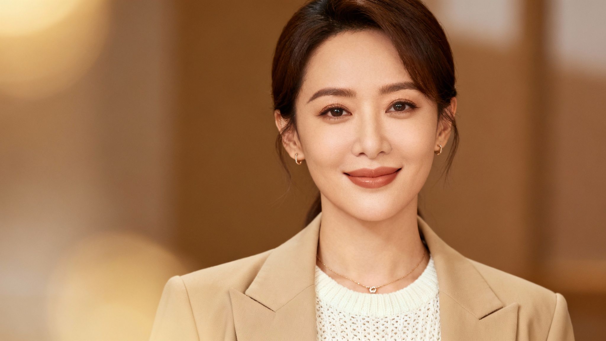 Professional woman in beige blazer and white sweater smiling at camera with warm lighting