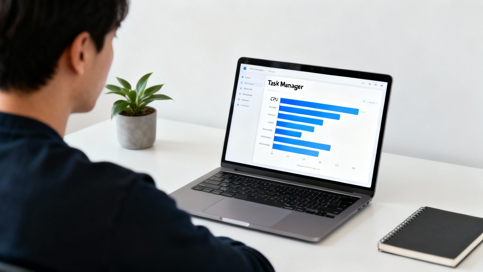 A person views a laptop screen displaying a task manager with CPU usage bars, next to a plant.