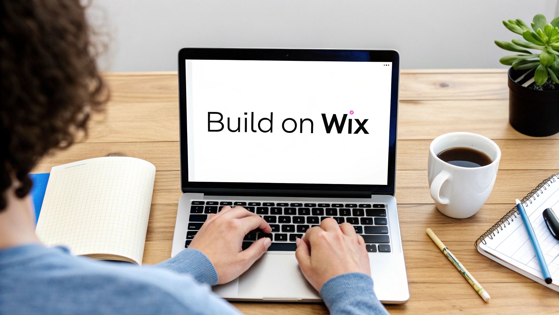 A person's hands typing on a laptop with 'Build on Wix' on the screen, on a wooden desk.